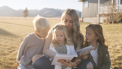 A mother reading The Book of Mormon Storybook with her children outdoors